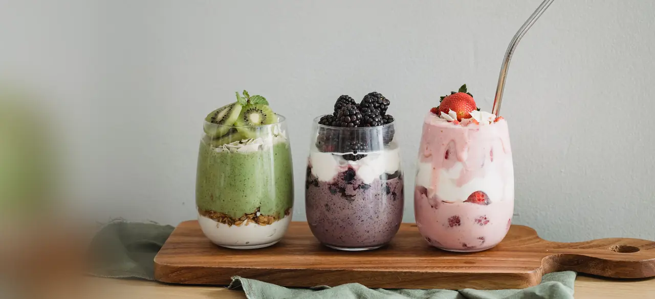 Três copos de vitamina em camadas com kiwi, amora e morango