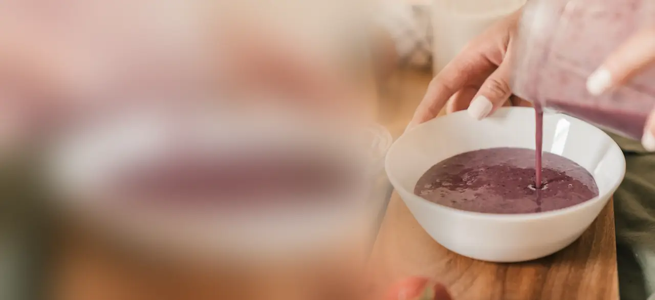 Vitamina de frutas vermelhas sendo servida do copo do liquidificador numa tigela branca