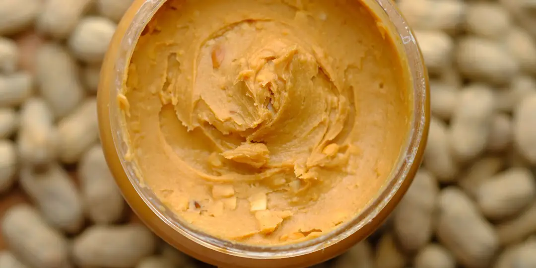 Pote de pasta de amendoim cremosa sobre amendoins