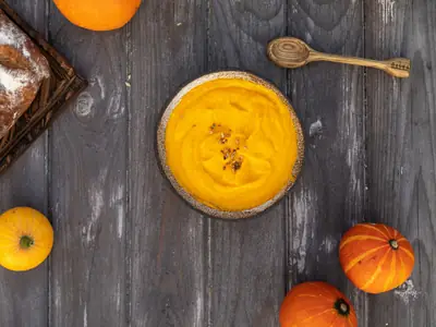 Creme de abóbora amarelo numa tigela, com abóboras pequenas ao lado