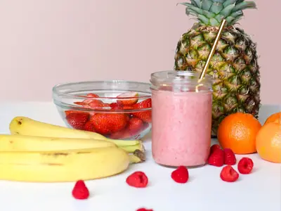 Vitamina rosa de morango e banana num pote de vidro, com bananas e morangos em volta